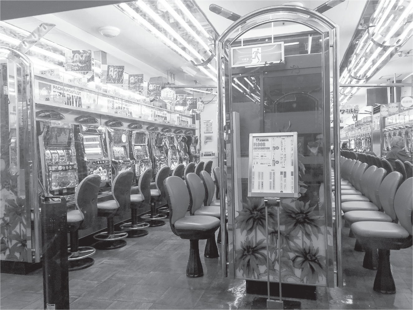 As if in a retro diner, red and orange plastic seats face pachinko and slot machines from another age. The machines are lit with sparkling purple, blue, and red lights.