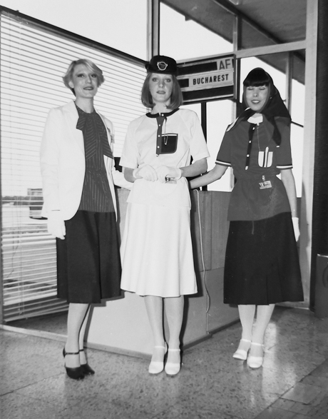 Figure 8.6. Three models wear prototype stewardess uniforms. One includes a white blazer and a blouse tied at the neck; one features a black bowler-style hat with a logo on the front along with a matching light-colored skirt and top set; and one has a red top and black skirt, shown with a scarf tied over the model’s hair. All include white gloves.