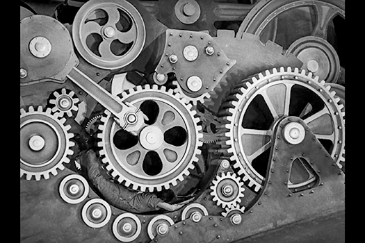 Figure 5.1. Film still showing wheels, cogs, and pulleys, as if we are seeing the inside of a clock. Charlie Chaplin's character the Tramp lies flattened beneath one of the wheels as his body is fed through the machine.