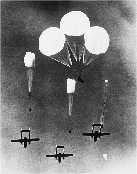 Figure 7. Three transport planes release equipment suspended by parachutes to drop to troops below.