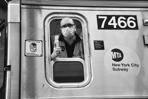 Figure 5. A masked transit worker gives a thumbs up as he leans from the window of a subway car marked with a decal that says, “Please keep a social distance.”