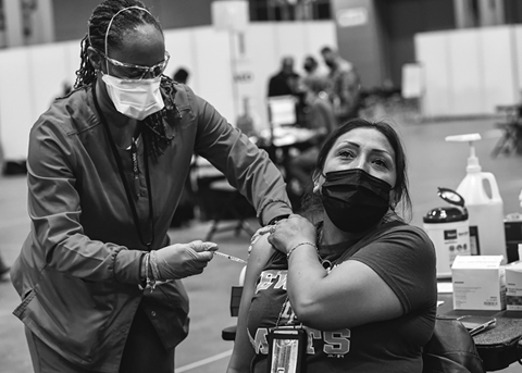 Figure 20. A transit worker wearing a mask looks upward as a masked woman vaccinates her.