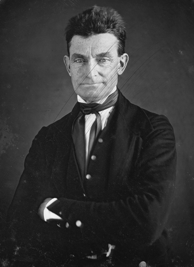 John Brown stands facing the camera, arms crossed and head high, his expression calm and clear. His clothes are plain, but his bearing is regally erect.