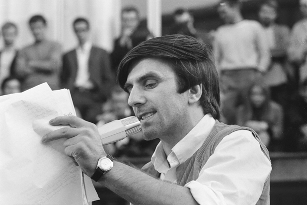 Figure 15. A young man, looking intense, speaks into a microphone. In his hand he holds the notes for his speech. In the background are the blurred figures of the people he is addressing.