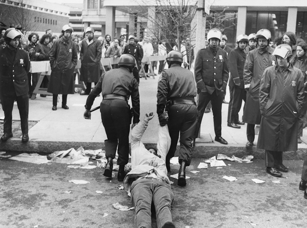 Figure 46. Two policemen in riot gear are dragging a protestor through police lines to arrest him. The protestor is lying on his back completely passive as the police haul him by his arms toward a group standing police.