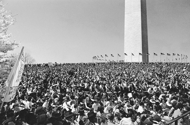 Figure 5. A crowd of 25,000 sit on the hill sloping up to the Washington Monument, which is circled by American flags. This is the first national protest of the Vietnam War.
