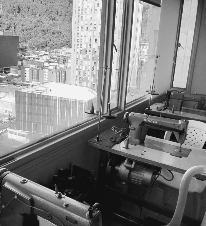 Figure 3.3. On the left, buildings and trees can be seen through a window on a high floor in a building. On the right, in front of the window, are tables with sewing machines.