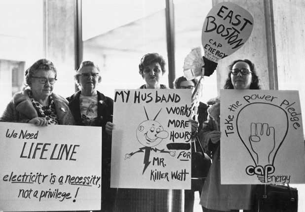 Figure 49. Five middle-aged and older white women hold signs saying, “We need lifeline, electricity is a necessity not a privilege,” “My husband works more hours for Mr. Killer Watt,” East Boston CAP-Energy,” and “Take the Power Pledge.”