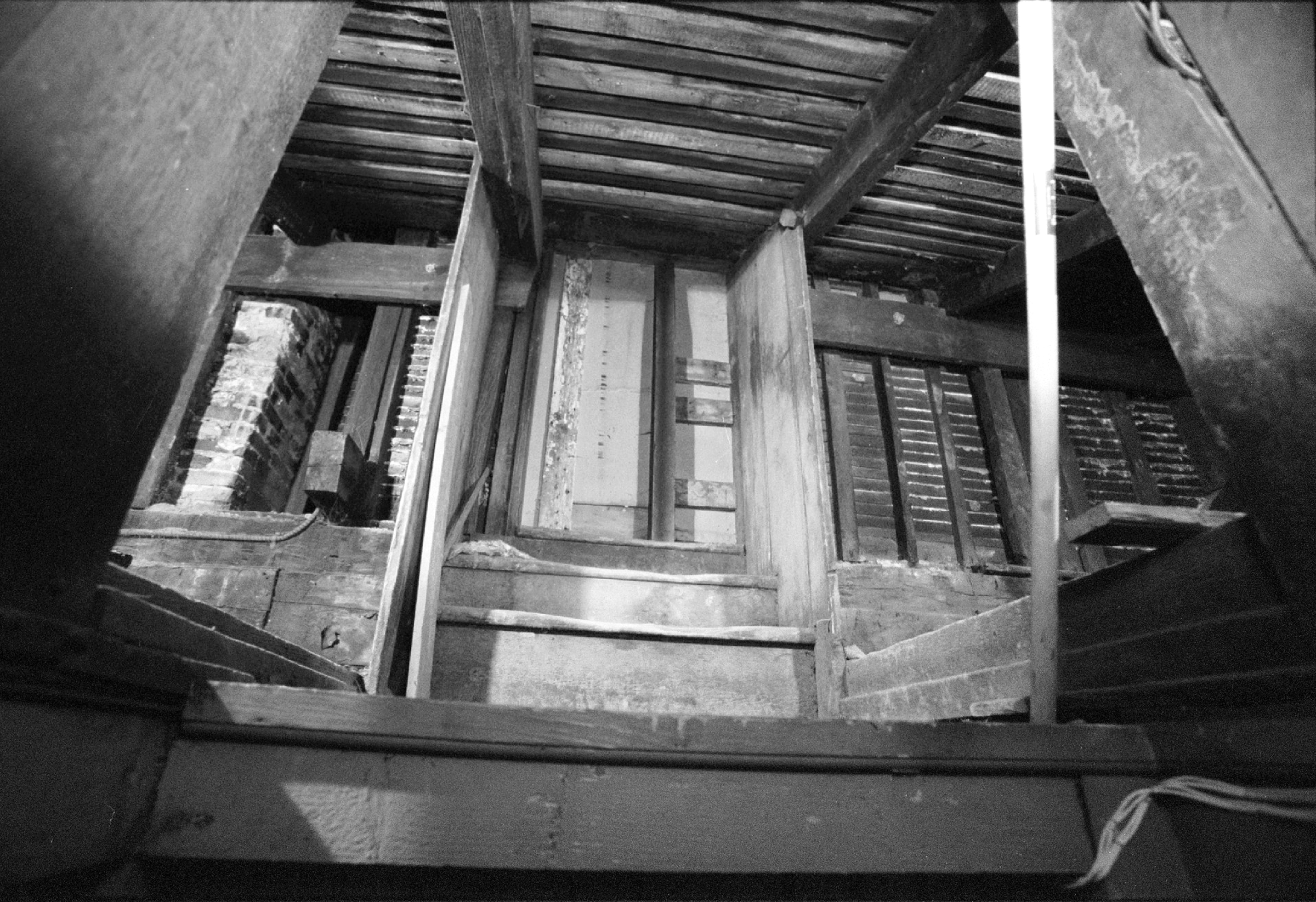 A photograph of stair steps that lead to a small door. On the side of the steps are entryways to garret spaces. There is no natural light in the image.