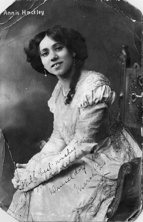 A portrait of a woman smiling in concert dress, her hands clasped over her crossed legs.