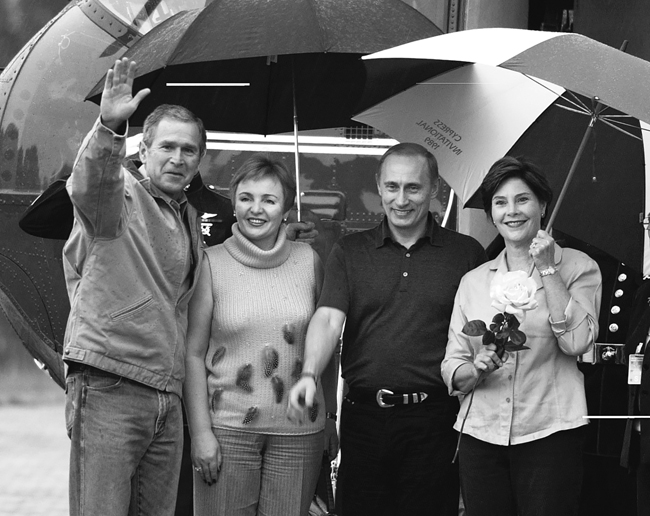 George W. Bush and Vladimir Putin with their wives smiling and standing under umbrellas, Crawford, Texas, November 2001.