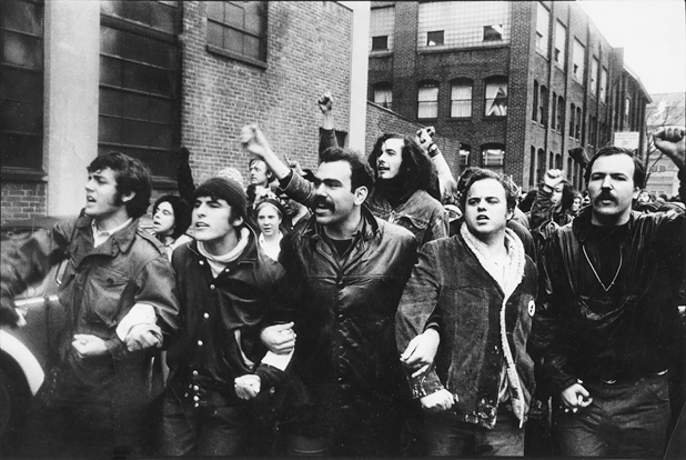 Figure 30. A line of young men, arms interlocked lead a march toward a confrontation with riot police. Behind marchers have fists raised. The mood is angry and militant.