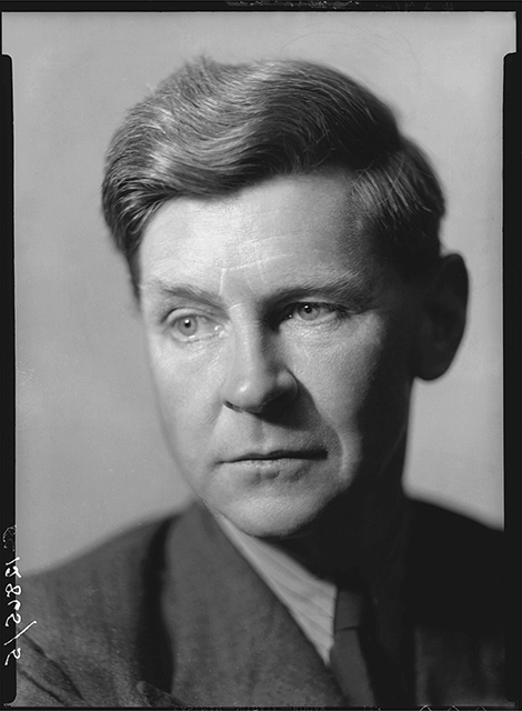 A closeup photo of a man wearing a suit with thick wavy hair.