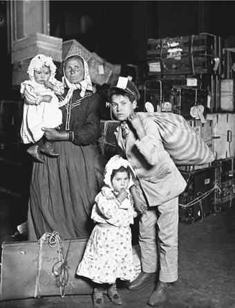 Figure 6.5. In a photograph taken in 1905 by Lewis Hine at the immigration reception hall on Ellis Island, an Italian immigrant family—mother, young son, and two little daughters—worries about missing luggage. Large piles of luggage are in the background.
