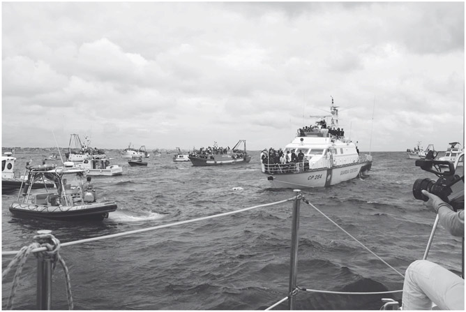 Figure 16. Approximately ten vessels circle a wreath of flowers floating on the sea. The closest boat is a Guardia Costiera vessel where groups of people stand on two levels.