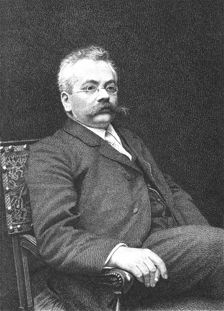 A man wearing a suit with a large, bushy mustache sits in a chair for a formal photograph.