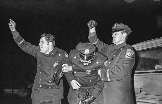 Figure 36. Two policemen are assisting another who is hurt. They are on each side of him, holding him up with one arm and their other arms are raised calling for help.